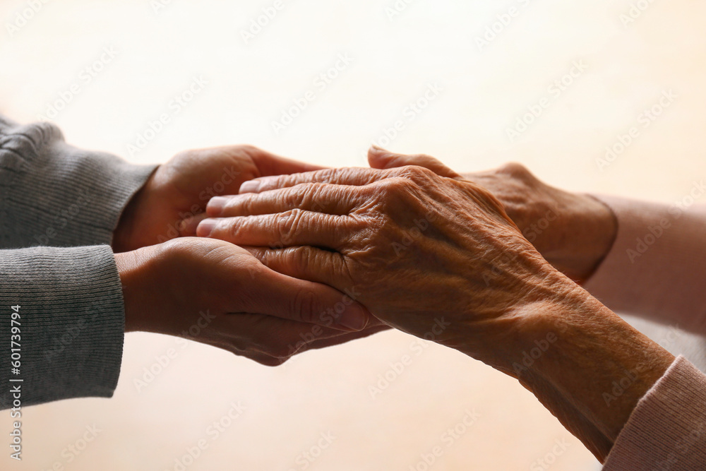 Fototapeta premium Cropped studio shot of elderly woman and female geriatric social worker holding hands. Women of different age comforting each other. Close up, background, copy space.