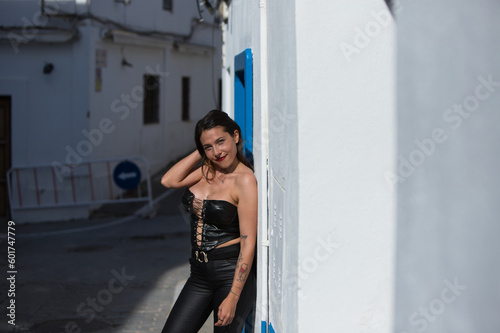Young and beautiful woman with long brown hair dressed in black leather leaning against the white wall of Conil. The woman is on holiday in spain in cadiz. The woman is happy.