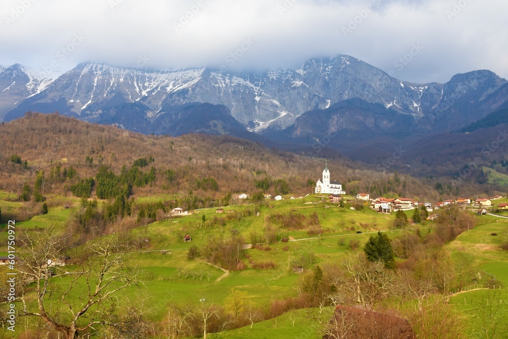 Scenic view of Drežnica village near Kobarid, Slovenia with the mountains in the Julian alps above covered in clouds and the meadows bellow lit by sunlight