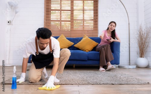 Asian man cleaning floor while lazy girlfriend doesn't help with housework. photo