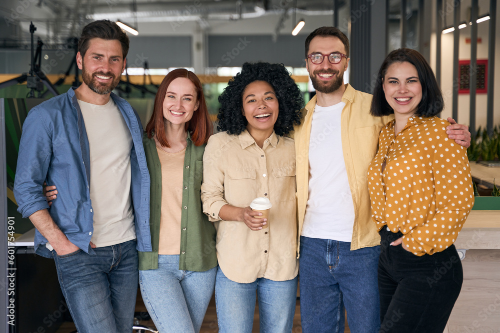 Group of happy multiracial business people, colleagues coworkers standing together in modern office. Portrait smiling stylish friends wearing casual clothes looking at camera. Diversity concept - obrazy, fototapety, plakaty 
