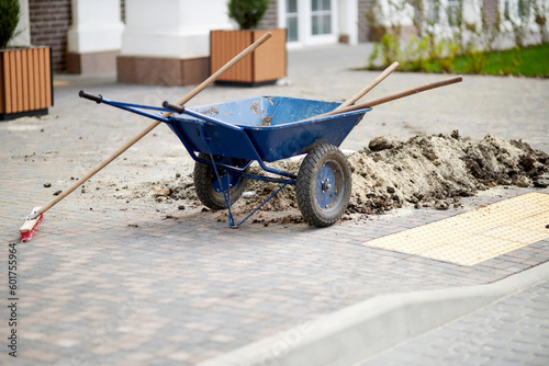 blue construction wheelbarrow with shovels. Blue iron wheelbarrow and gray cobblestones. metal wheelbarrow with a shovel on the street.