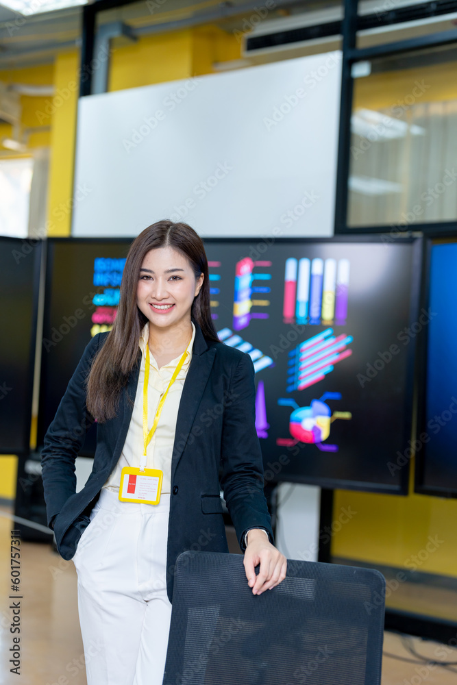 Fototapeta premium Successful businesswoman standing in creative office and looking at camera. Woman entrepreneur in a coworking space smiling. Portrait of beautiful business woman standing