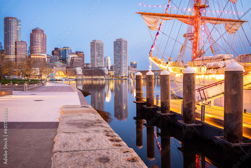 View of Boston in Massachusetts, USA at The fan Pier and Boston Harbor at sunrise showcasing the skyline of the city and a vintage sailing boat anchored on the side.