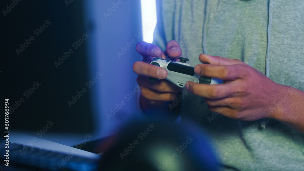 Close up of man gamer hands holding joystick for play console game. Young Middle East Asian male using wireless controller playing game to win highest score victory sit in neon light RGB living room