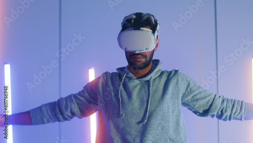 Young Middle East man putting on Virtual Reality headset for first time exploring VR world express amazed, surprised feeling of strange future atmosphere sit in RGB neon light gaming room