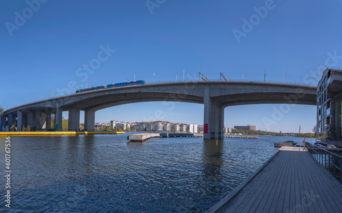 The bay at the Essinge islands in the sea Mälaren, a tram passing on a high way bridge and waterfront modern apartment houses, a sunny early summer day in Stockholm