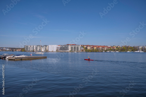 The bay at the Essinge islands in the sea Mälaren, a canoe and a sailing boat passing and modern apartment houses, an sunny early summer day in Stockholm © Hans Baath