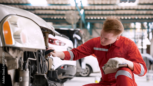 mechanic is checking front car, which enters garage in wrecked state, mechanic checks condition, writes it down in book, before taking it for repairs speed clearly know where repair.