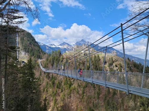 People walking across swinging bridge to historic medieval castle in Austrian Alps - Austria
