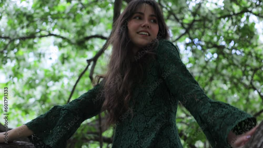 A young woman is sitting on a branch of a blossom apple tree in the forest. Vertical video A young woman is sitting on a branch of a blossom apple tree in the forest. Vertical video