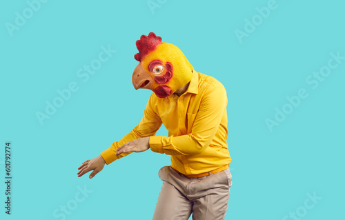 Funny crazy man with chicken head dancing isolated on pastel light blue background. Man in absurd rubber mask of chicken head has fun during costume party. Creative advertising concept.