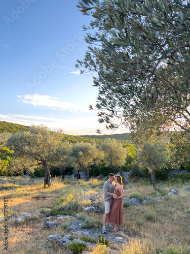Embracing man and woman stand on dry grass in a green olive grove © Nadtochiy