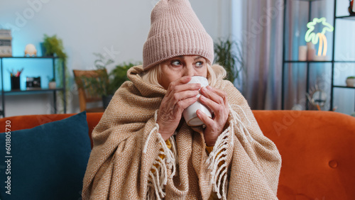 Fotografía Sick senior grandmother woman in plaid shivering from cold on sofa drinking hot tea in unheated apartment without heating due debt