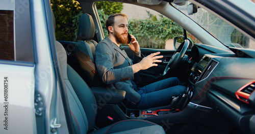 Attractive businessman young male in auto speaking on mobile phone and smiling.. Cheerful casual man sitting in luxury car and chatting on smartphone.