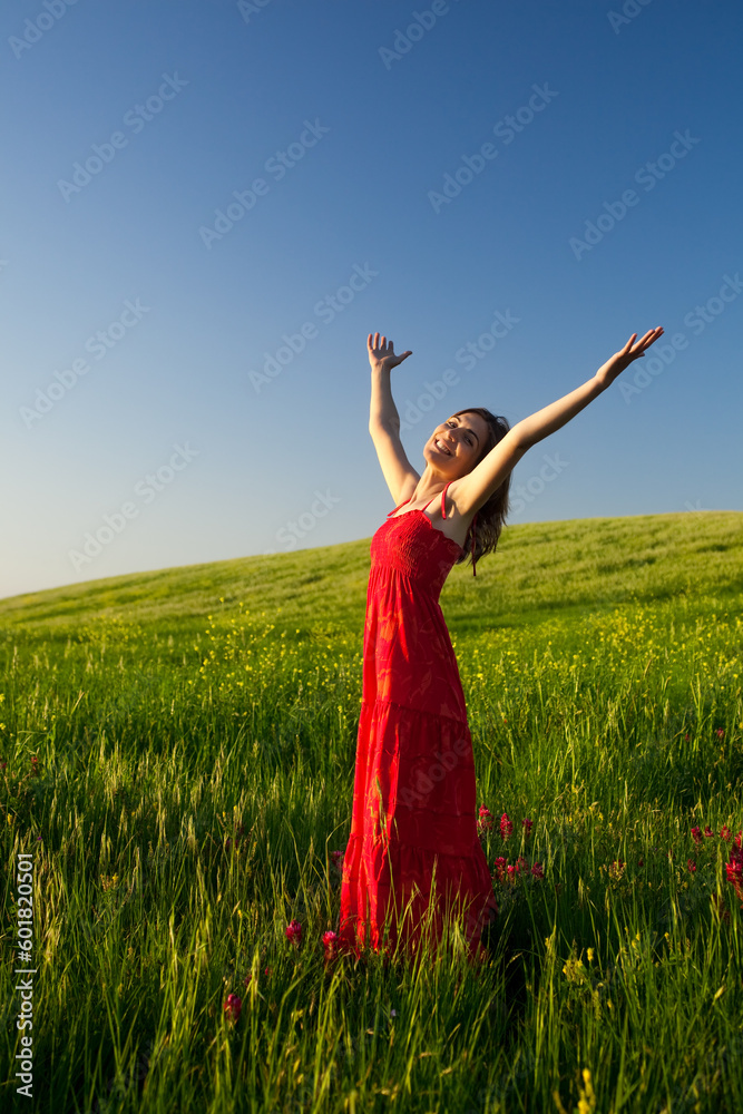Beautiful young woman relaxing on the field with both arms open