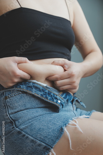 Close up of a belly with scar from c-section and abdominal fat. Women's health. A woman dressed up in sportswear demonstrating her imperfect body after a childbirth with nursery on the background.