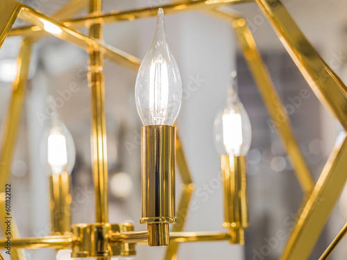 Luminous ceiling shade made of yellow gold metal with transparent glass lamps in the form of candles. Concept of interior decoration. Inside. Close up. Evening light. © Anna Shnaider