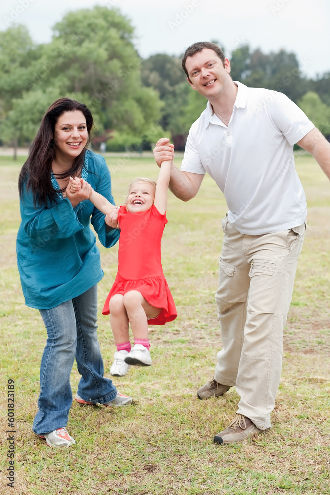 Lovely couples playing with their happy daughter at the park over natural background Lovely couples playing with their happy daughter at the park over natural background