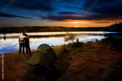 A pair of campers with a tent set against a beautiful sunset lake landscape