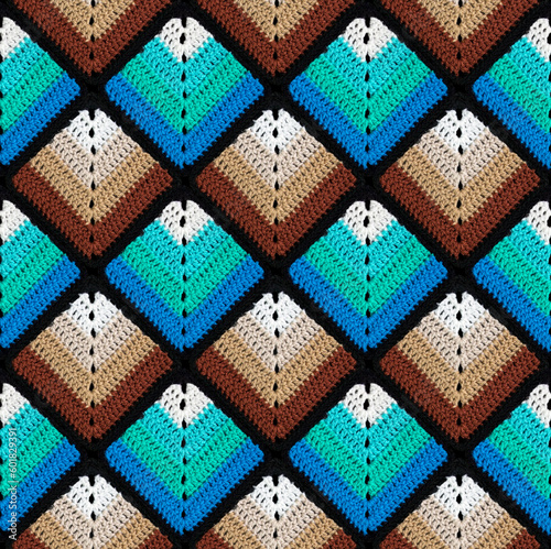 Seamless knitted pattern in the form of gradient rhombuses is crocheted with multi-colored threads. Patchwork style. Acrylic blanket.