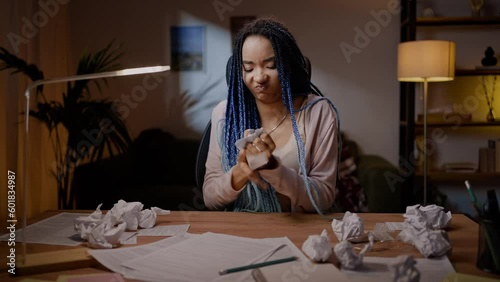 Woman sitting at desk with crumpled paper sheets, experiencing lack of inspiration writing article photo