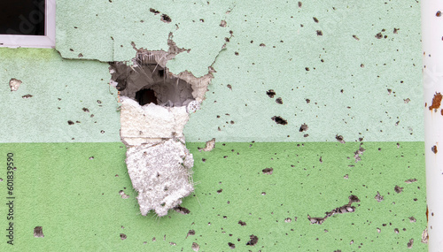 Holes from bullets and shrapnel in the wall on the front line. Scars of war. Concrete wall of a residential building with potholes and holes from gunfire. Consequences of the war in Ukraine.