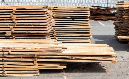 Pile of stacked wooden planks at a construction site. Wooden boards  lumber. Industrial edged timber. Wooden rafters for the repair or construction of a private house. Roofing and joinery lumber.