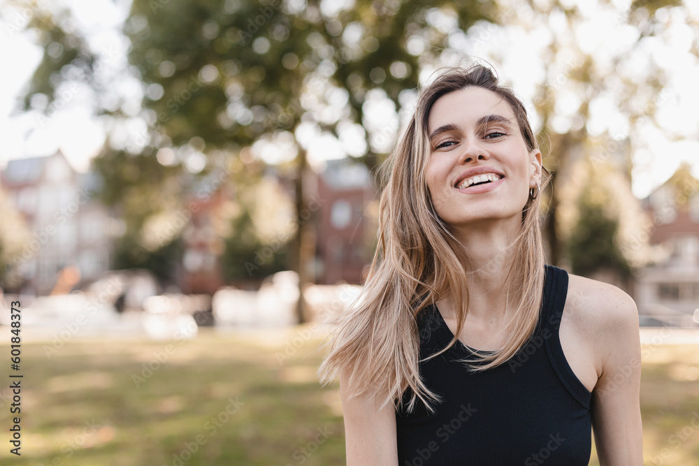 Beautiful woman smiling and look at camera in countryside. Outdoor portrait of a smiling blonde girl. Happy cheerful girl laughing at green city, look fashion and show toothy smile. She wear black top Beautiful woman smiling and look at camera in countryside. Outdoor portrait of a smiling blonde girl. Happy cheerful girl laughing at green city, look fashion and show toothy smile. She wear black top