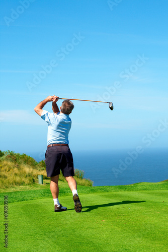 Senior male golfer playing golf from the tee box facing the ocean on a beautiful summer day