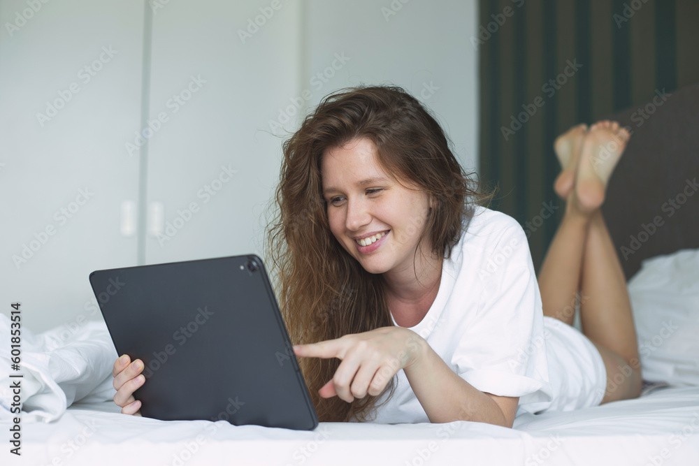 Happy young woman is using tablet computer at home in bed in bedroom, smile, have fun Happy young woman is using tablet computer at home in bed in bedroom, smile, have fun