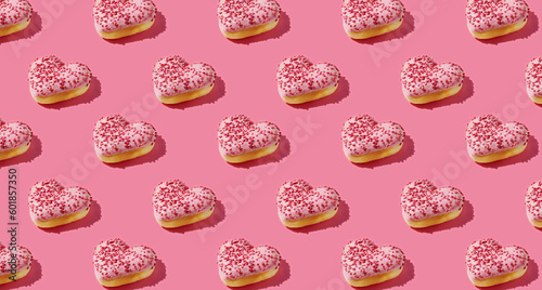 Pattern of heart shaped pink donut with glaze on pink pastel background