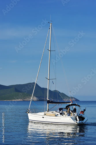 Sailing yacht with two people approaching a remote Greek island in early morning