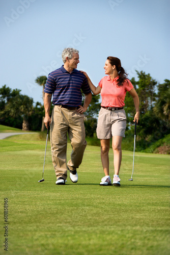 Caucasion mid-adult man and woman walking on golf course talking to each other.