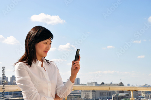 young businesswoman looking on the mobile phone in left hand, outside, space for copy and text