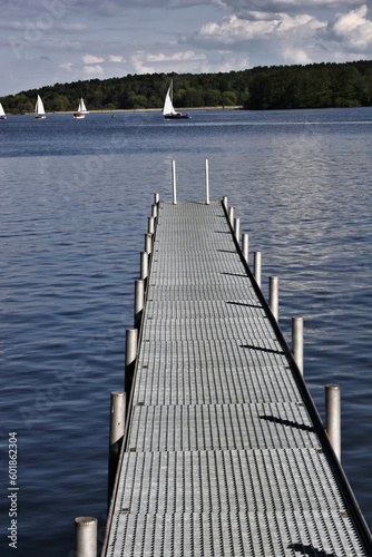 footbridge reaches into a lake with sailing boats in the background