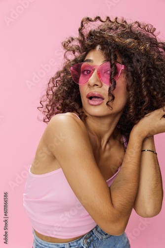 Happy woman afro curls hair dancing on pink background smile with teeth in summer pink t-shirt jeans and glasses, summer vibe, copy space