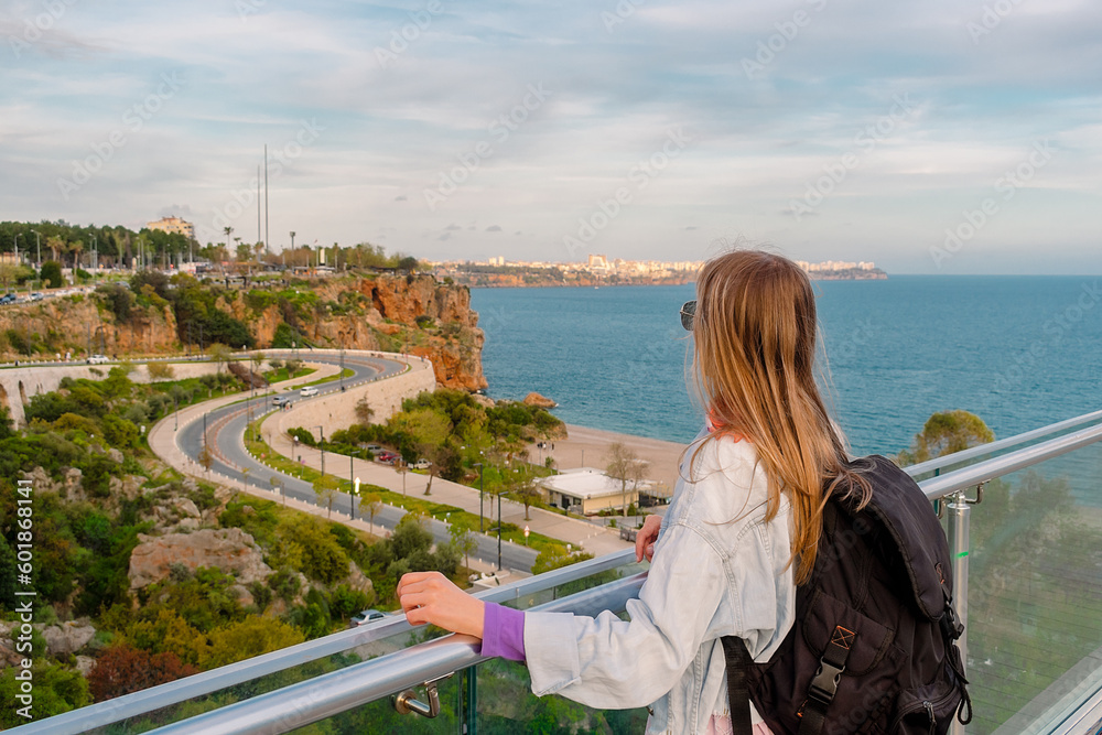 A tourist girl stands on a viewing platform. A girl with a backpack looks at the beach in the city of Antalya.