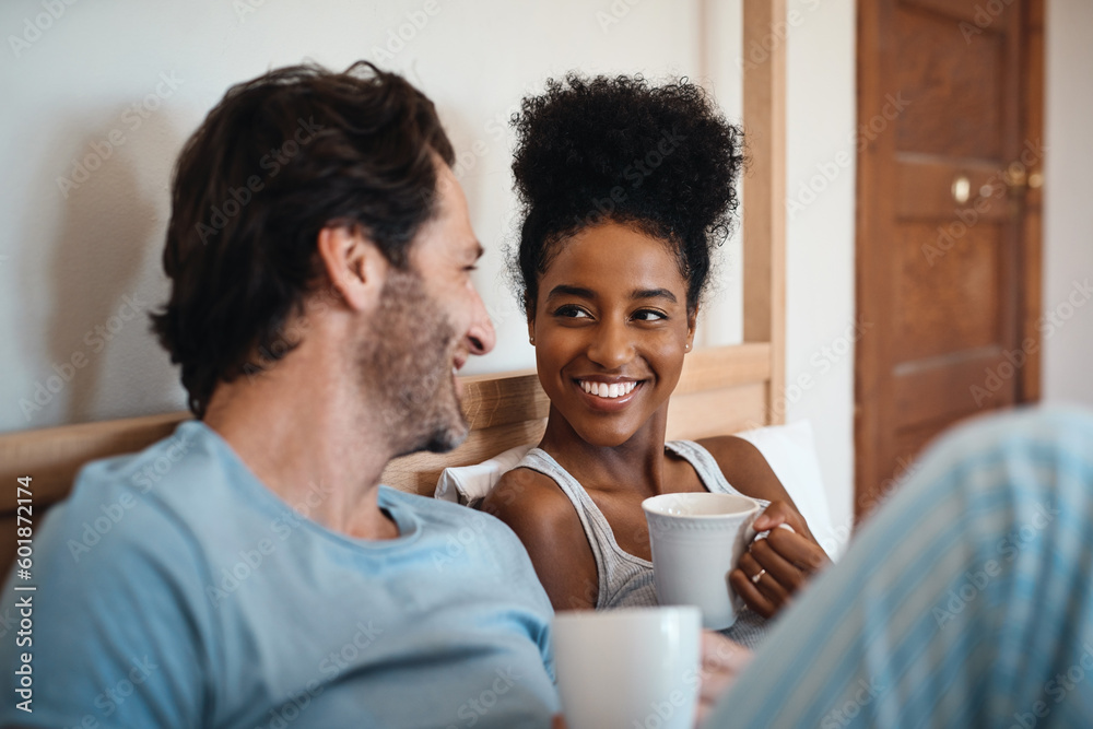 Happy interracial couple, bed and coffee in relax for morning, bonding or breakfast at home. Man and woman smiling for tea, conversation or talk on relaxing weekend or holiday together in the bedroom