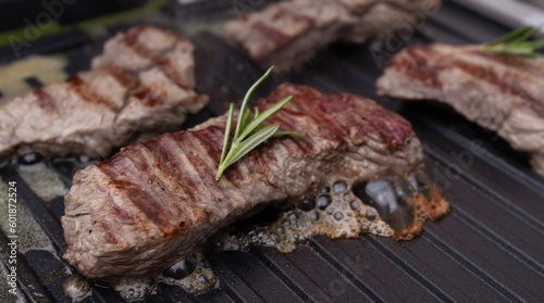 meat beef steak on electric grill cooked, with fresh rosemary. The meat is roasted with stripes. hot photo with steam. grill season