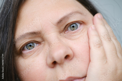 close up part mature female face, woman 50-55 years old looks carefully examines wrinkles around eyes, hanging eyelid, age-related changes, aesthetic injection cosmetology, care anti-aging procedures