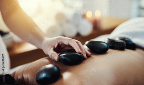 Woman, hands and rocks in relax for back massage, skincare or beauty relaxation on bed at spa. Hand of masseuse applying hot rock or stones on female for physical therapy or treatment at a resort
