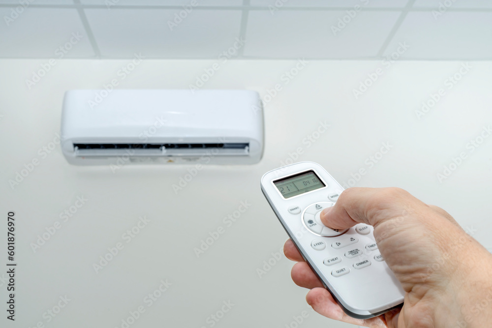 HAND ADJUSTING AIR CONDITIONER TEMPERATURE WITH REMOTE CONTROL. ENERGY SAVING AND EFFICIENCY. ENERGY POVERTY CONCEPT.