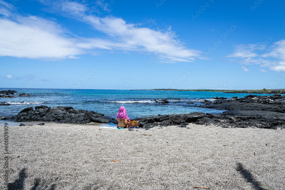 Photo of a woman in a bikini with a bright pink wrap covering her head from the sun on an empty beach on the Big Island of Hawaii. Photo of a woman in a bikini with a bright pink wrap covering her head from the sun on an empty beach on the Big Island of Hawaii.