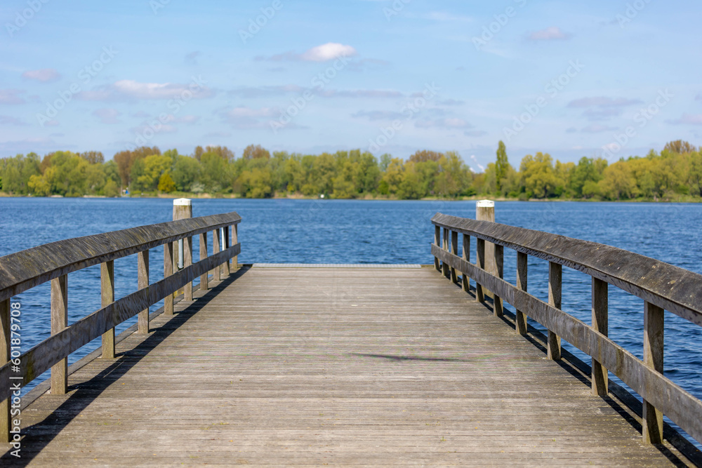 Spring landscape with wooden jetty (pier) extend into the Nieuwe meer (New lake) Beautiful sunny day with white fluffy clouds and blue sky background, Amsterdamse Bos (Forest) Amstelveen, Netherlands.