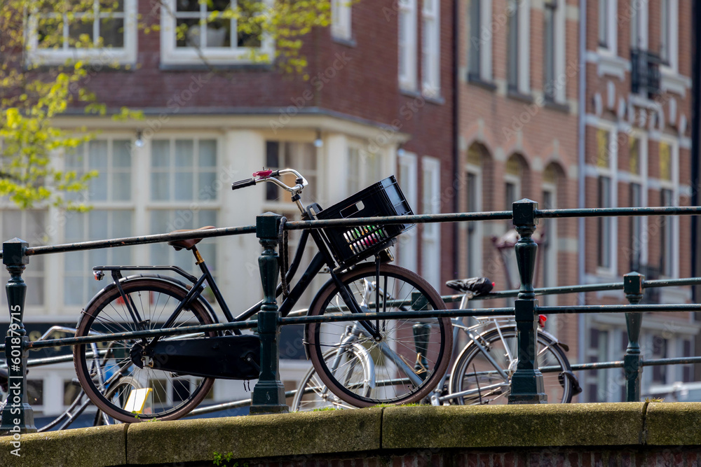 Selective focus of classic bicycle and handlebar on canal bridge in the evening with warm sunlight, Blurred traditional houses, Amsterdam, Netherlands, Cycling is a common mode of transport in Holland