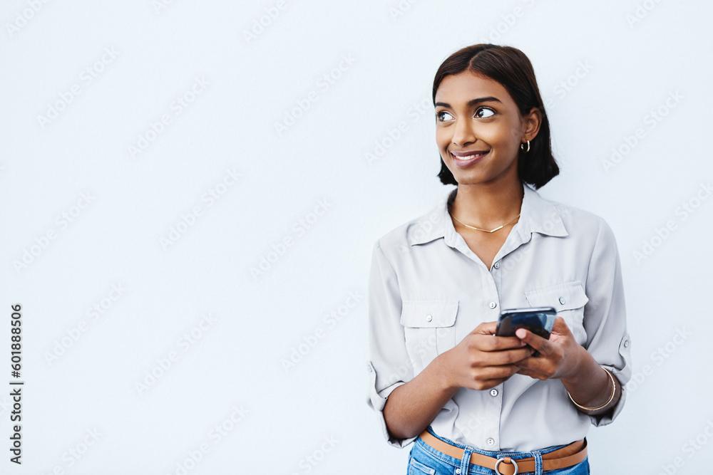 Social media, young Indian woman on smartphone and thinking in studio background. Smiling or idea, phone for communication or networking and happy female person standing with cellphone in backdrop Social media, young Indian woman on smartphone and thinking in studio background. Smiling or idea, phone for communication or networking and happy female person standing with cellphone in backdrop