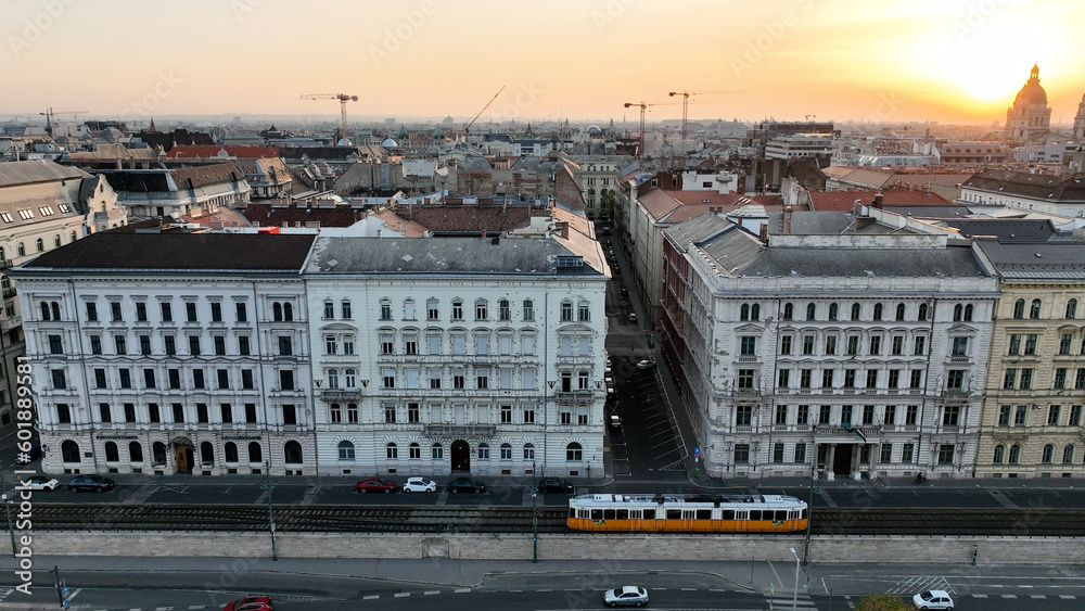 Typical Budapest Tram passing through city neighbourhood in beautiful golden hour Sunrise light, Aerial tracking follow shot wide angle