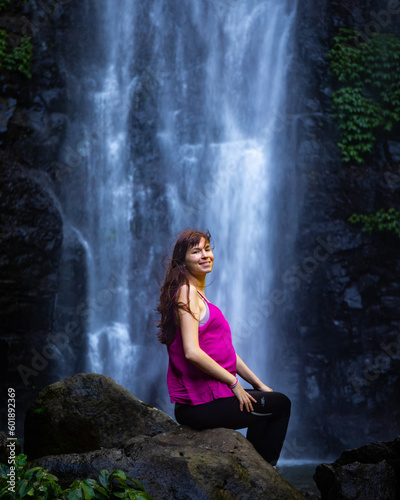 beautiful girl sitting in front of large tropical waterfall - larapinta falls in lamington national park near gold coast, queensland, australia