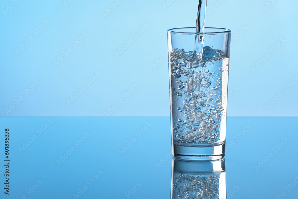 Pouring water into glass on light blue background. Space for text Pouring water into glass on light blue background. Space for text